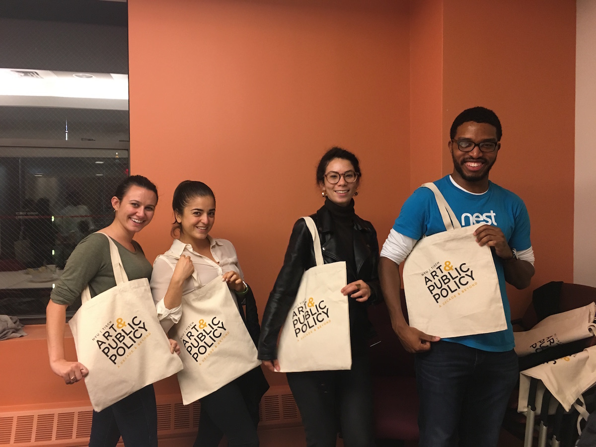 Four people hold canvas tote bags that read "Art & public Policy: A Decade and Beyond"